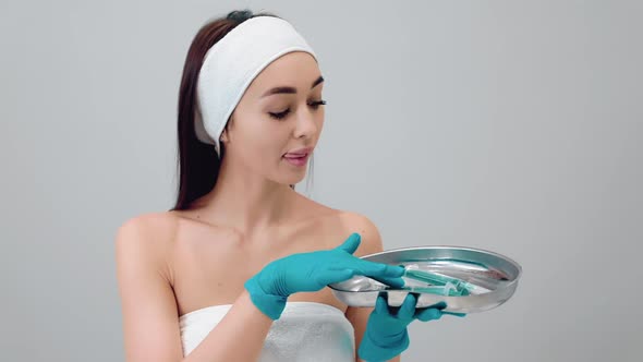 Portrait of a young beautiful woman in medical gloves choosing syringes from medical kidney dish.