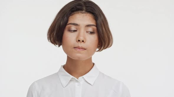 Young Beautiful Brunette East Asian Female in Shirt Standing on White Background Undecided Shying in