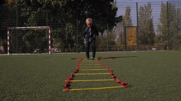 A Little Boy Trains on the Football Field He Performs an Exercise on the Ladder