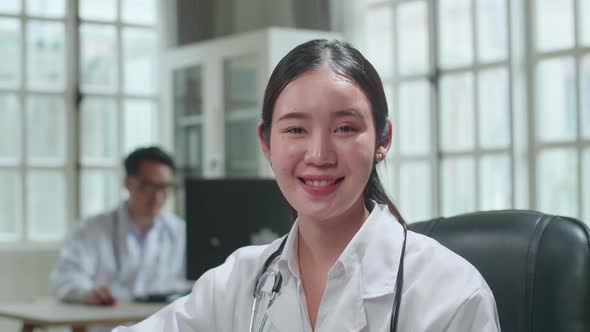 Young Asian Woman Doctor Is Using Computer, She Turns And Smiles To Camera In Workplace