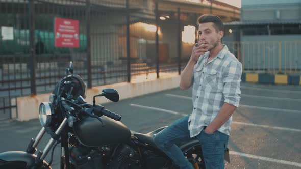 Portrait of Man Motorcyclist Smokes a Cigarette While Sitting on a Motorcycle at Street