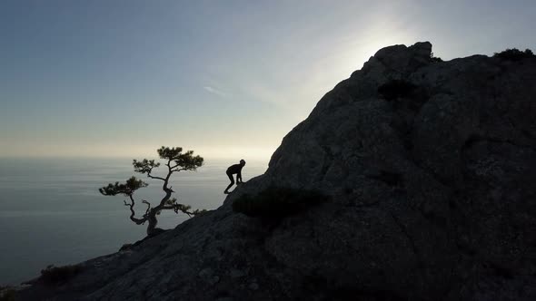 Aerial Silhouette of Young Woman Climbing Up To the Top of a Mountain in Front of the Sea. Flight