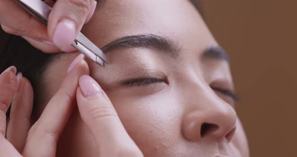 Cosmetologist Tweezing Eyebrows of Young Asian Woman Before Make Up