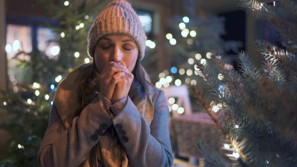 Portrait of a Happy Woman Against the Backdrop of Christmas Decorations. She Rubs Her Hands, Keeping