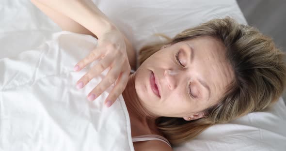 A Woman Wakes Up and Looks in Surprise Under a White Blanket