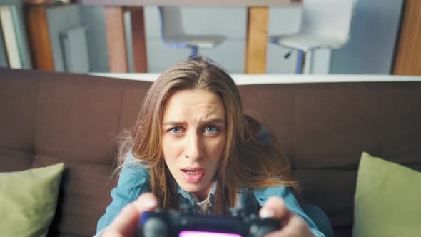 A Beautiful Excited Young Gamer Girl is Sitting on a Couch and Playing Video Games on a Console