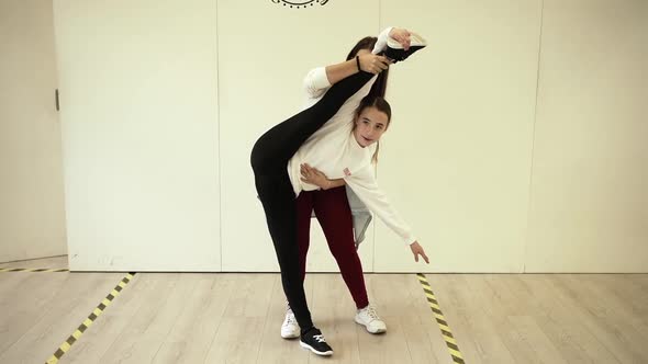 Female instructor helping girl with stretching legs in studio