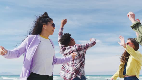 Happy group of diverse female friends having fun, dancing and smiling at the beach