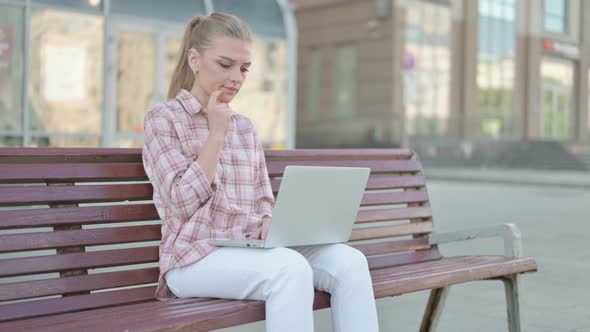 Thinking Young Woman Using Laptop While Sitting Outdoor on Bench