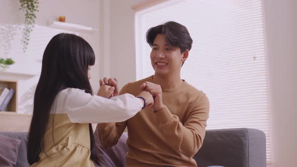 Asian father teaches daughter to play games and do activities on the sofa on vacation.