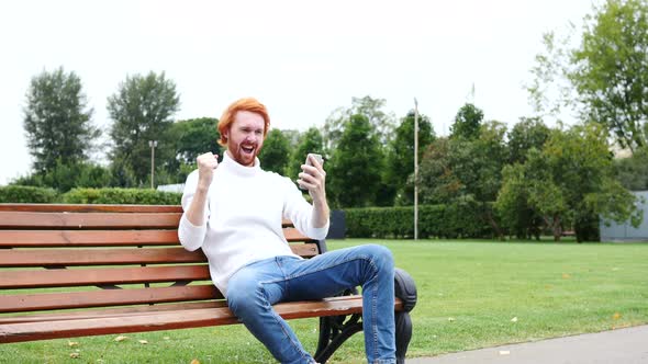 Man Excited for Success, Using Smartphone, Sitting on Bench