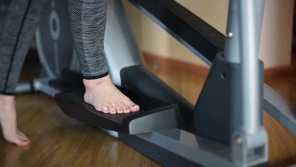 A barefoot girl stands on the pedal of an ellipsoid and begins training