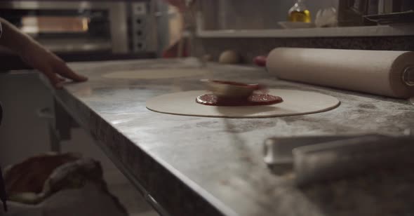 Crop chef smearing tomato sauce on pizza