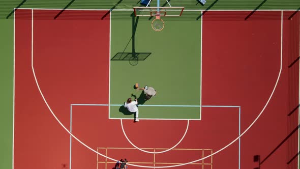 Aerial View of Two Young Male Friends Playing Basketball on Court Outdoors and Cameraman Filming