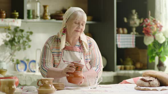 Grandmother Pouring Milk Into the Glass From Crock in the Country