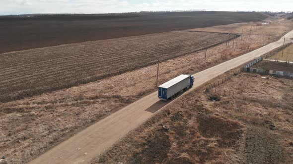 Aerial View of a Large Truck with a Trailer Driving Along a Dirt Road in Search of a Place for a U