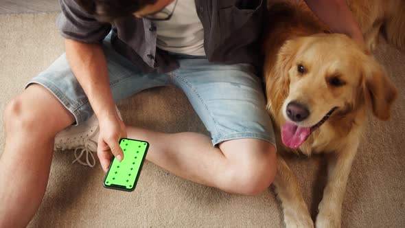 Young Man in Glasses Petting Golden Retriever Sitting on Floor in Livingroom