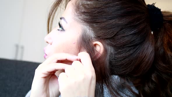 Close Up Of A Woman Putting On Her Heart-shaped Earring While Sitting.