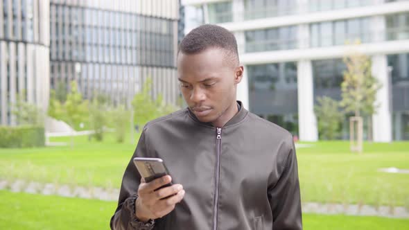 A Young Black Man Takes Selfies with a Smartphone - Office Buildings in the Blurry Background