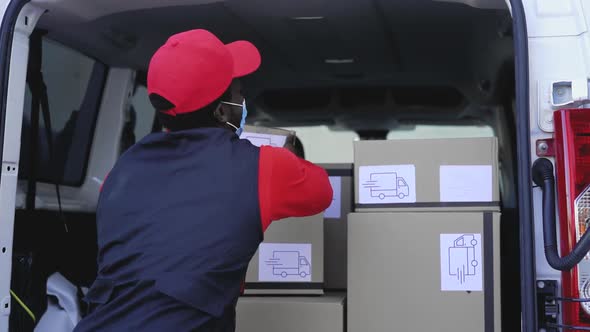 African delivery man loading boxes in the truck while wearing face mask