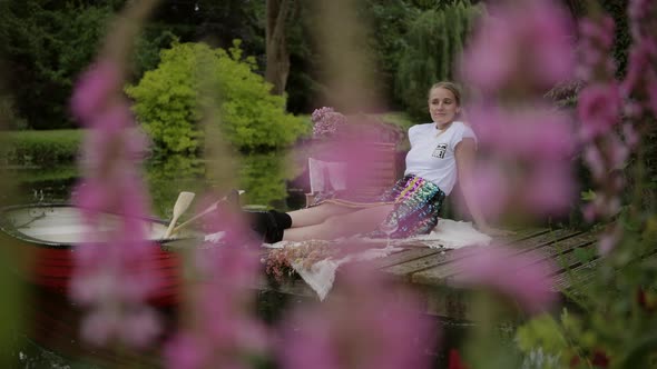 Woman relaxes on wooden jetty at botanical garden with pink flower in foreground