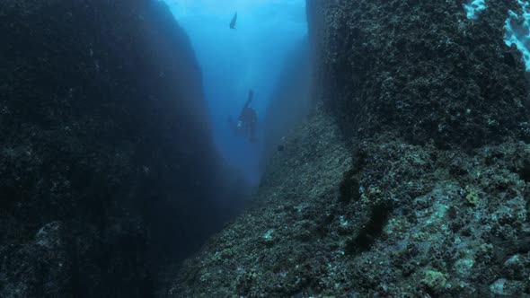 Silhouette of a group of divers exploring a large rock crevice deep in the ocean. Wide underwater vi
