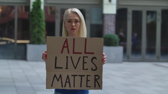 Outdoors Portrait of a Young White Female Activist Holding a Cardboard Poster with an Inscription