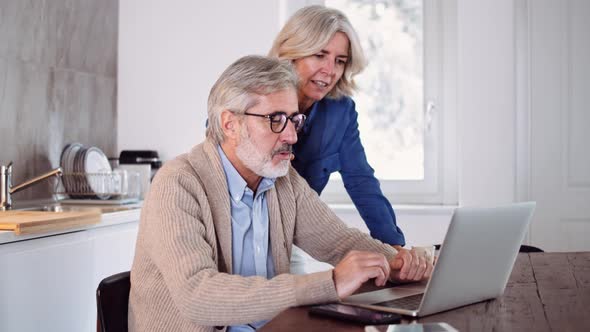 Slow motion shot of mature couple using laptop at table in the kitchen