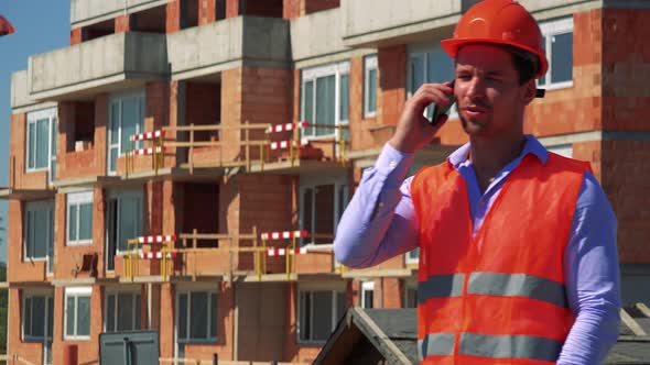 Construction Worker Phones with the Smartphone in Front of Building Site