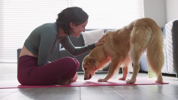 Caucasian woman keeping fit and sitting on yoga mat with dog