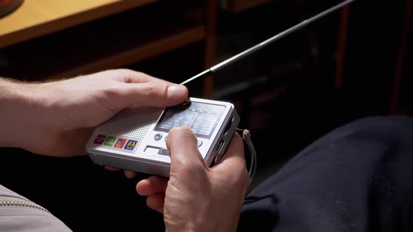 A Male Tunes a Radio Frequency on a Small Receiver with an Antenna