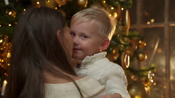 Loving Mother Holds Her Little Son in Her Arms Hugs Standing Near the Christmas Tree
