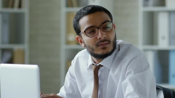 Thoughtful Middle Eastern Businessman Typing on Laptop