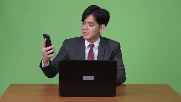 Young Handsome Asian Businessman Working with Laptop Against Green Background