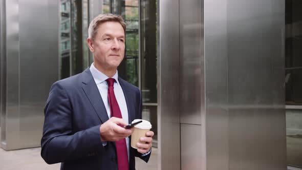 Businessman walking to work using smart phone with takeaway coffee