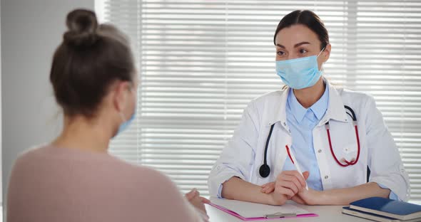 Young Female Doctor Wearing Protective Mask Talking to Senior Patient