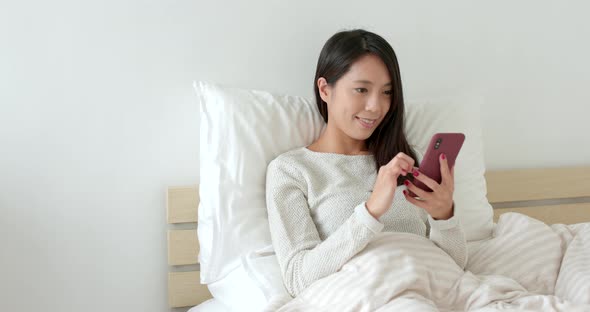 Woman sending audio message with smart phone and sitting on bed