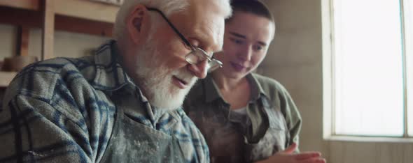 Elderly Sculptor Giving Lesson to Young Woman in Workshop