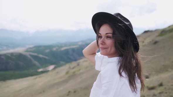 Attractive Brunette in a Hat and White Shirt Is Enjoying Nature in the Mountains. Beautiful Young