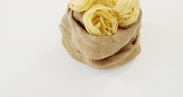 Raw tagliatelle pasta in hessian sack on white background