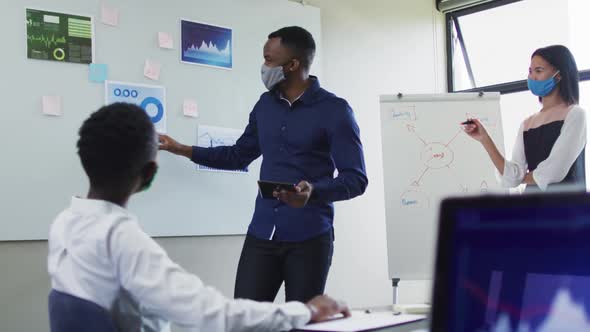 African american man and woman wearing face masks giving presentation to their colleagues in meeting