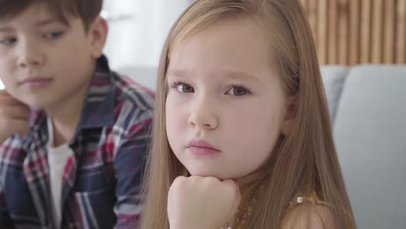 Close-up Portrait of Sad Caucasian Girl with Brown Eyes Looking at Camera and Away As Blurred Boy