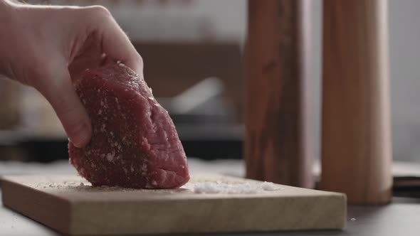 Slow Motion Slide Shot of Man Rubbing Raw Beef Steak with Spices on Oak Board Closeup