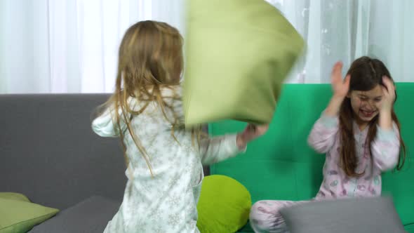 Two Little Girls Fighting with Pillows on Sofa