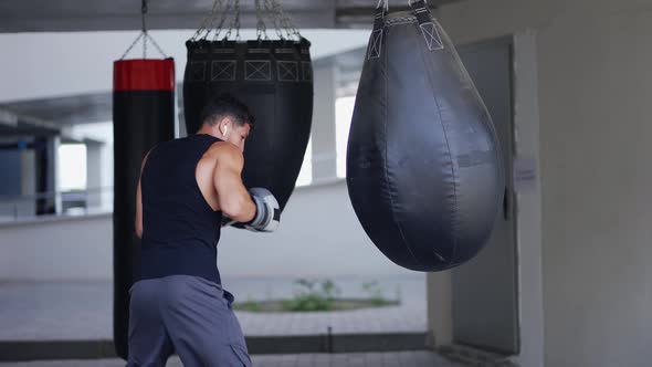 The Man Executes Strong Blows in the Boxing Bag Outdoors