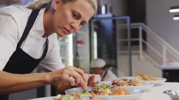 Caucasian female chef wearing chefs whites in a restaurant kitchen,putting food on a plate