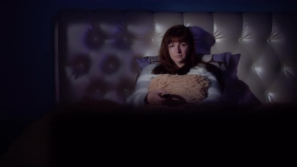 Brunette Woman Lies in Bed in the Evening and Watches Tv with Emotion