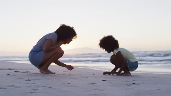 African american mother and daughter playing in the sand together at the beach