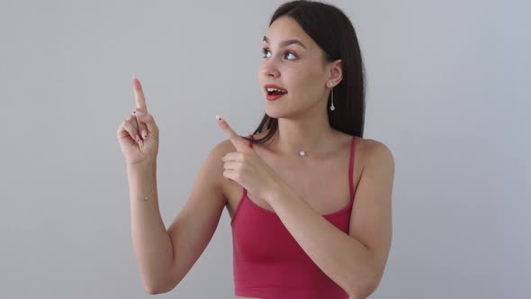 Pretty Young Female in Red Clothes Points Up and Joyful Waves Hands to Camera