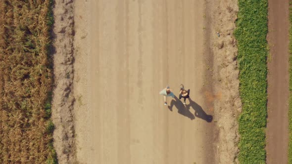 A Young Man and a Girl Jog Along a Dirt Road Next To Green and Cereal Fields.